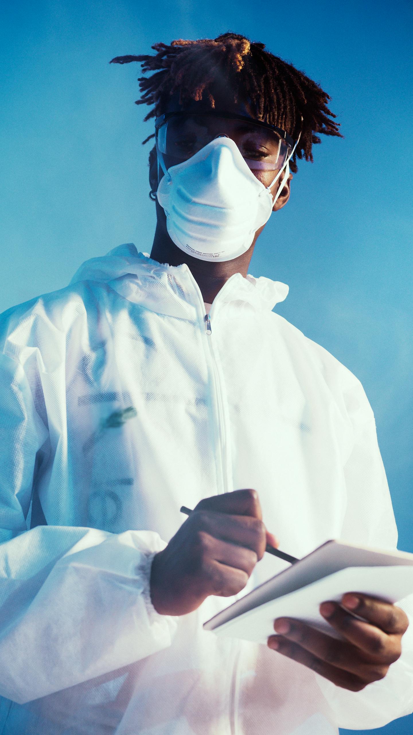 Healthcare professional in protective gear taking notes, blue sky background, concept of scientific research and safety.